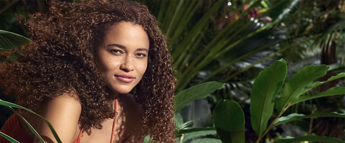 model with curly in hair in front of leaf background